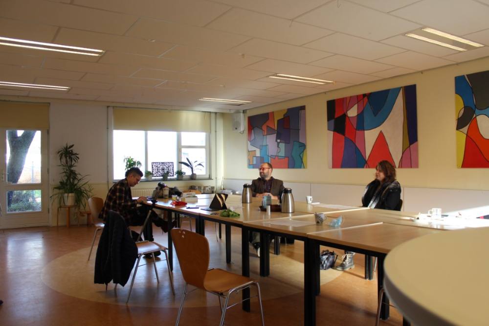 De grote zaal met lange tafels en kleurrijke kunst aan de muur